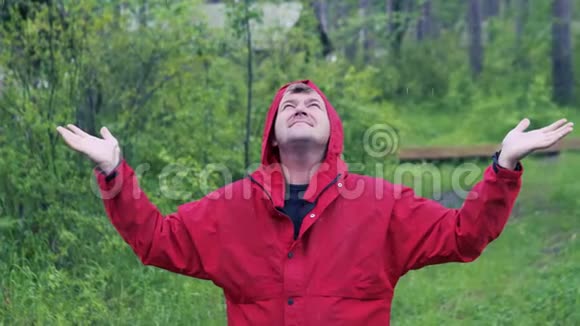 一个人站在雨中在一片绿色森林的背景下张开双臂站在一边视频的预览图