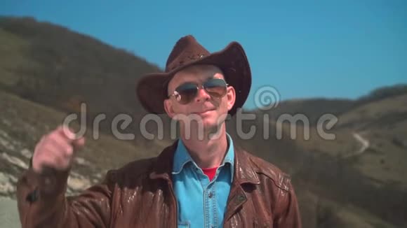戴牛仔帽皮夹克眼镜的人一个人把手放在帽子上脱下帽子视频的预览图