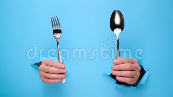 用手握住勺子用叉子穿过撕裂的蓝色纸墙吃饭的手势视频的预览图
