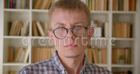 白种人图书管理员专注而严肃地看着镜头把眼镜固定在书架上的画像视频的预览图