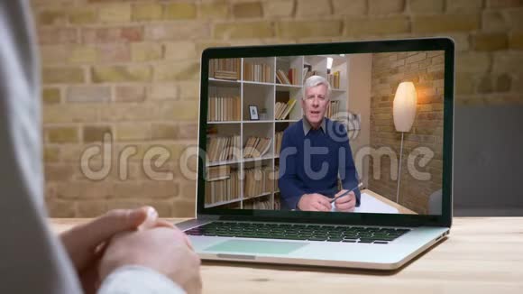 在线采访高级专家用铅笔和笔记本认真地与他的搭档在屏幕后面交谈视频的预览图