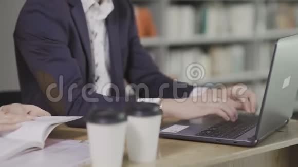 年轻英俊的男人在图书馆的笔记本电脑上工作桌上有一杯咖啡视频的预览图