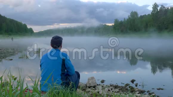 人坐在地上看着平静的河水雾视频的预览图