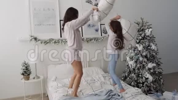快乐无忧无虑的妈妈和学龄前女孩在床上享受一场有趣的枕头大战妈妈和女儿把枕头翻了三倍视频的预览图