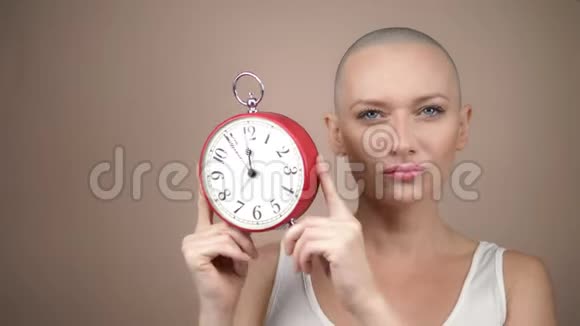 美丽的秃头女人手里拿着闹钟和粉红色的丝带温和的粉彩背景视频的预览图
