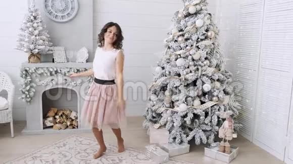 美丽的女孩子在圣诞树附近微笑着穿着漂亮的裙子在装饰的房子里跳舞新年快乐视频的预览图