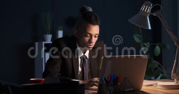 睡眼的商人在夜间办公室里伸展身体使用笔记本电脑视频的预览图