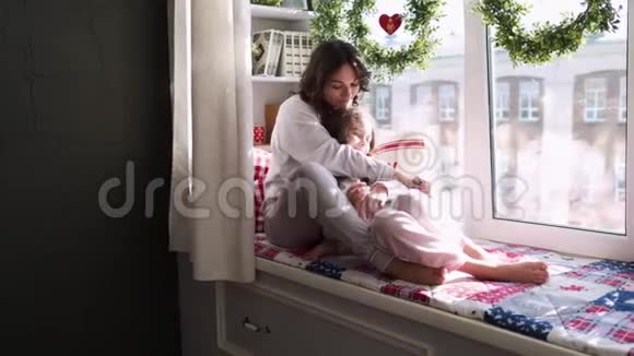 妈妈和女儿正坐在窗前的圣诞装饰背景上幸福的家庭妈妈和宝宝视频的预览图