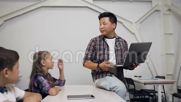 可爱的白种人女学生和同学坐在桌子后面举手向韩国人提问视频的预览图