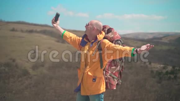 一个穿着黄色夹克和眼镜的人站在山上欣赏风景在视频中交谈视频的预览图