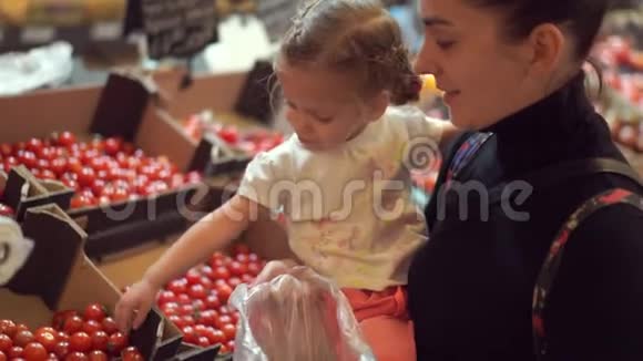 妈妈抱着她的小女儿在超市里摘西红柿商店里的买家视频的预览图