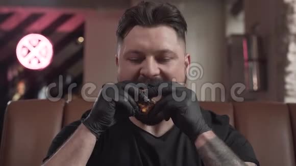 一个戴着黑手套的留胡子的人坐在咖啡馆的皮革沙发上吃着美味的汉堡那个人视频的预览图