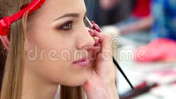 化妆师在一家美容院里化妆画一个年轻女孩的眼睛手里拿着一支画影子的画笔视频的预览图