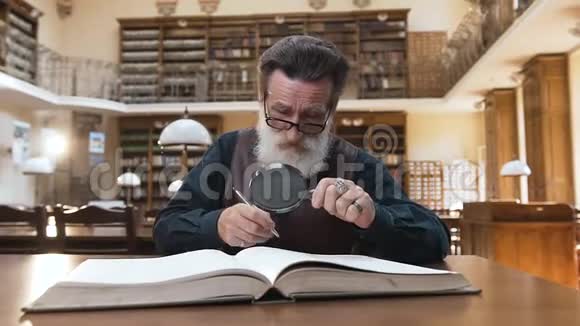 一个戴眼镜戴胡子的人在图书馆桌上看书视频的预览图