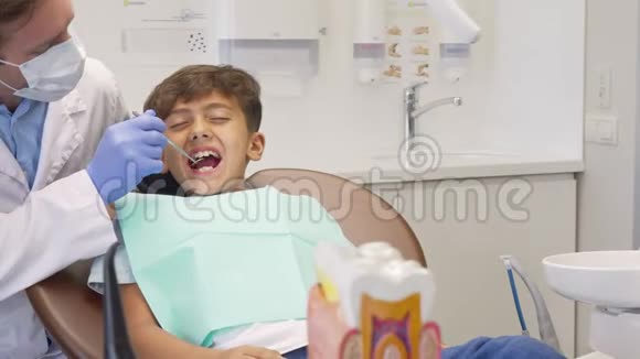 年轻的男孩看起来很害怕正在成熟的牙医检查他的牙齿视频的预览图