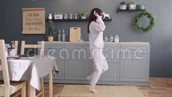 快乐的年轻女子穿着睡衣在厨房跳舞早上在家听音乐和咖啡视频的预览图