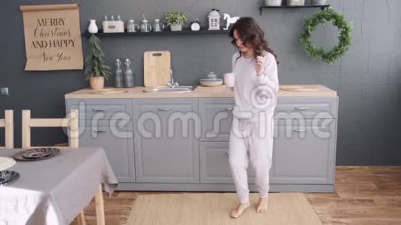 穿着睡衣的年轻女子在厨房里喝了早晨的咖啡后正在听音乐跳舞视频的预览图