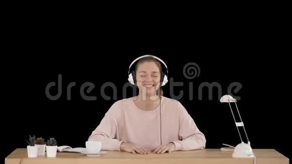 穿着粉色套头衫的漂亮女士戴着耳机听音乐对着镜头微笑阿尔法频道视频的预览图