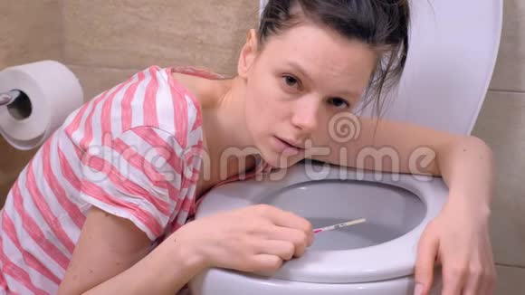 晨吐年轻的孕妇疲惫的女人在家里的厕所里呕吐看着镜头视频的预览图