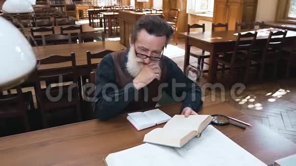 吸引人的是专注于看书的留胡子戴眼镜的老人坐在图书馆的桌子旁拿着书视频的预览图