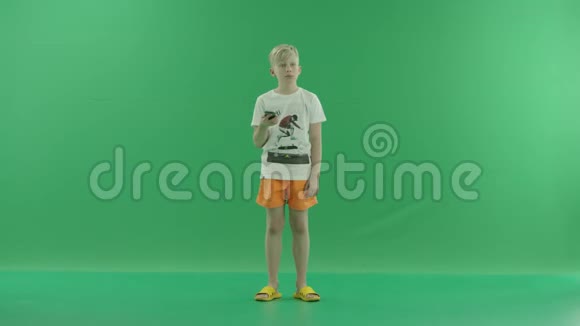 穿着休闲服的快乐金发男孩正在打手机他靠着一块绿色的屏幕站在前面视频的预览图