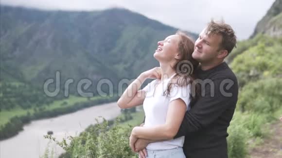 一个男人拥抱一个女人他们朝一个方向看从山上看到一个美丽的景色视频的预览图