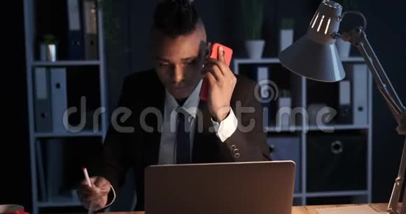 商务人员在夜间办公室用手机和笔记本做笔记视频的预览图