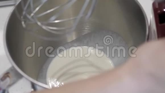 女性手将红色搅拌器浸入金属碗中加入白色液体并打开视频的预览图