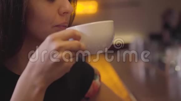 一位迷人的年轻女子坐在酒吧柜台旁享受着她的咖啡并随着音乐而移动漂亮姑娘视频的预览图
