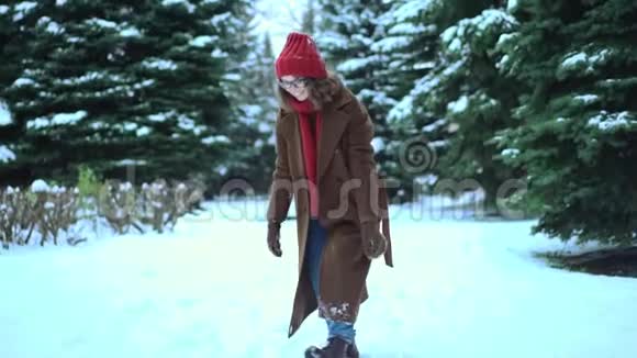穿着针织围巾和帽子的年轻漂亮女人在公园里玩雪球冬季时尚视频的预览图