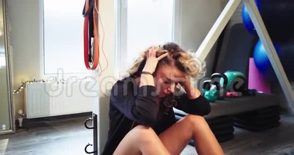 在一个健身房里一位女士在锻炼后坐在地板上在辛苦的一天之后把头发抬起放松一下视频的预览图