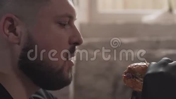 一个戴着黑手套吃美味汉堡的留胡子男人的侧面画像那个人在里面吃着令人垂涎的快餐视频的预览图