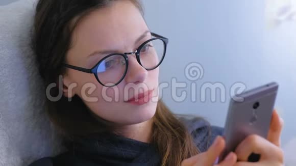 戴眼镜的女人正在智能手机上浏览和寻找社交媒体视频的预览图