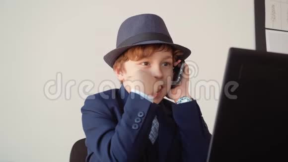 小男孩在办公室用手机前笔记本电脑打电话年轻商人在智能手机上聊天视频的预览图