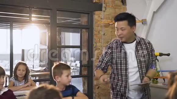小学的男韩裔教师在课桌之间行走把数字平板电脑放在桌子上而一组视频的预览图