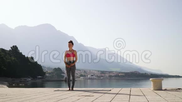 成人健身妇女在空海码头做瑜伽背景是山脉视频的预览图