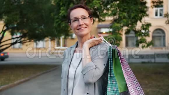 慢镜头肖像成熟女士拿着购物袋微笑在外面视频的预览图