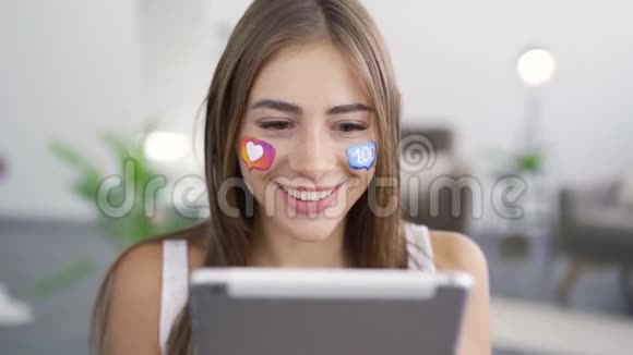 年轻美丽的高加索女人的肖像脸上画着社交媒体图标手里拿着平板电脑视频的预览图