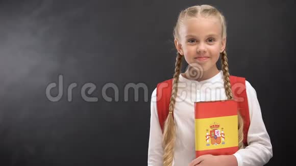 微笑的女学生拿着西班牙语书在黑板的背景下视频的预览图