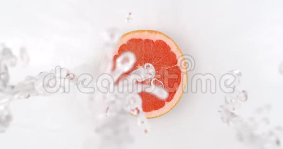 俯视图在白色的背景上一个新鲜的葡萄柚躺在水里水滴从上面落下从上面落下视频的预览图
