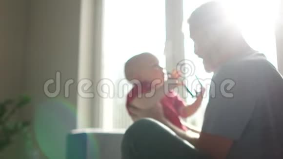 好爷爷把小孙子抱在窗户对面的房间里夕阳太阳耀斑幸福的家庭视频的预览图