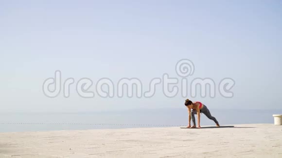 运动女性在石头上做瑜伽背景是大海和天空视频的预览图