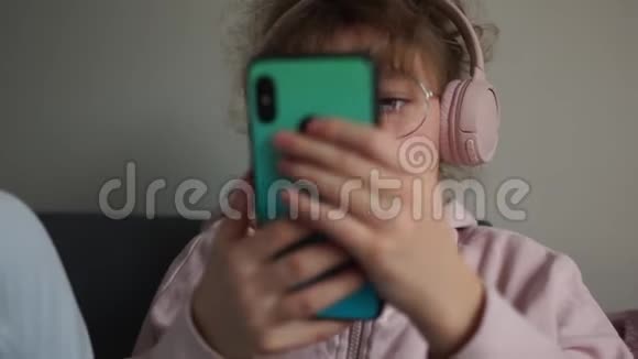 戴着眼镜和无线耳机的可爱少女的肖像手里拿着智能手机的女孩视频的预览图