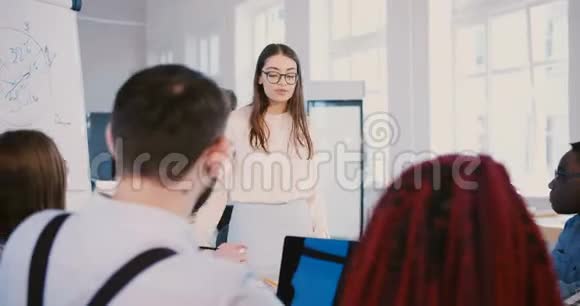 年轻的千禧商业女性戴着眼镜与专业的混合种族团队的初创公司合作伙伴交谈视频的预览图