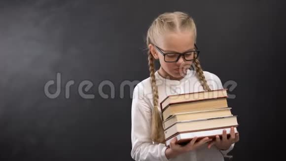 戴眼镜的聪明的女学生几乎不把书堆在黑板上视频的预览图