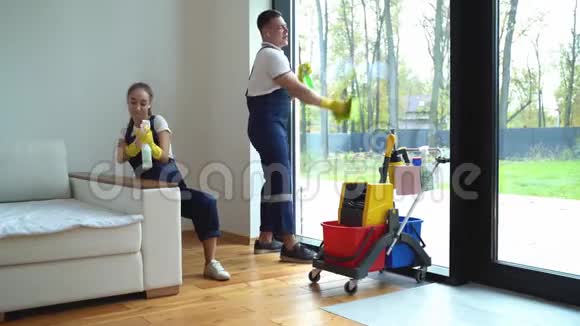 年轻妇女和男子从清洁服务穿着工作服和橡胶手套在家里跳舞视频的预览图