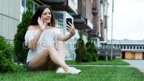 美女通过手机视频聊天坐在草地上和朋友说话视频的预览图