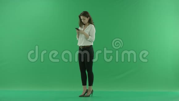 一位身穿便服的快乐美女正站在绿色屏幕前一边用手机聊天视频的预览图