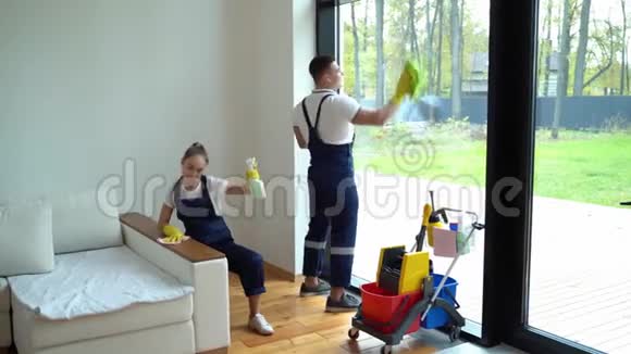 年轻妇女和男子从清洁服务穿着工作服和橡胶手套在家里跳舞视频的预览图