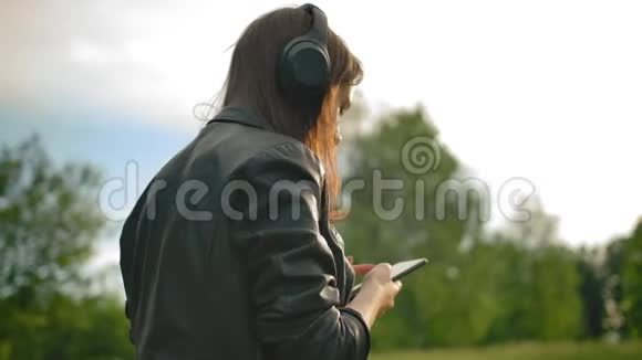 女孩用智能手机听wifi耳机的音乐和她的狗在公园里散步视频的预览图
